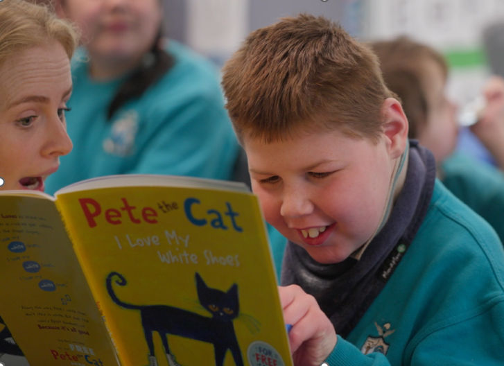 Young boy reading a book called Pete the Cat